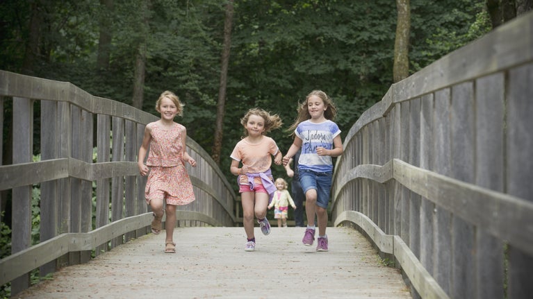 Three girls running across the bridge at Llanerchaeron in Ceredigion, Wales